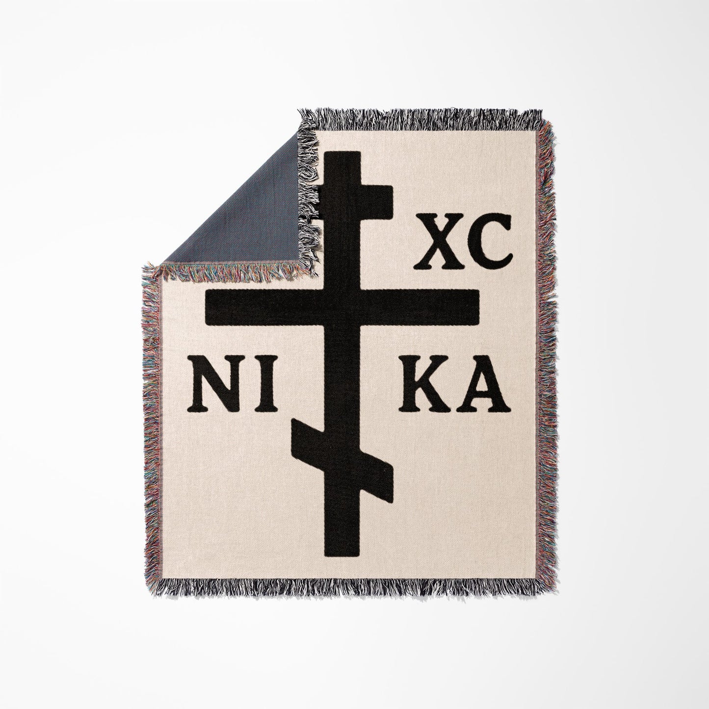 Black Orthodox Christian cross with "NI XC KA" text on a fringed throw blanket.