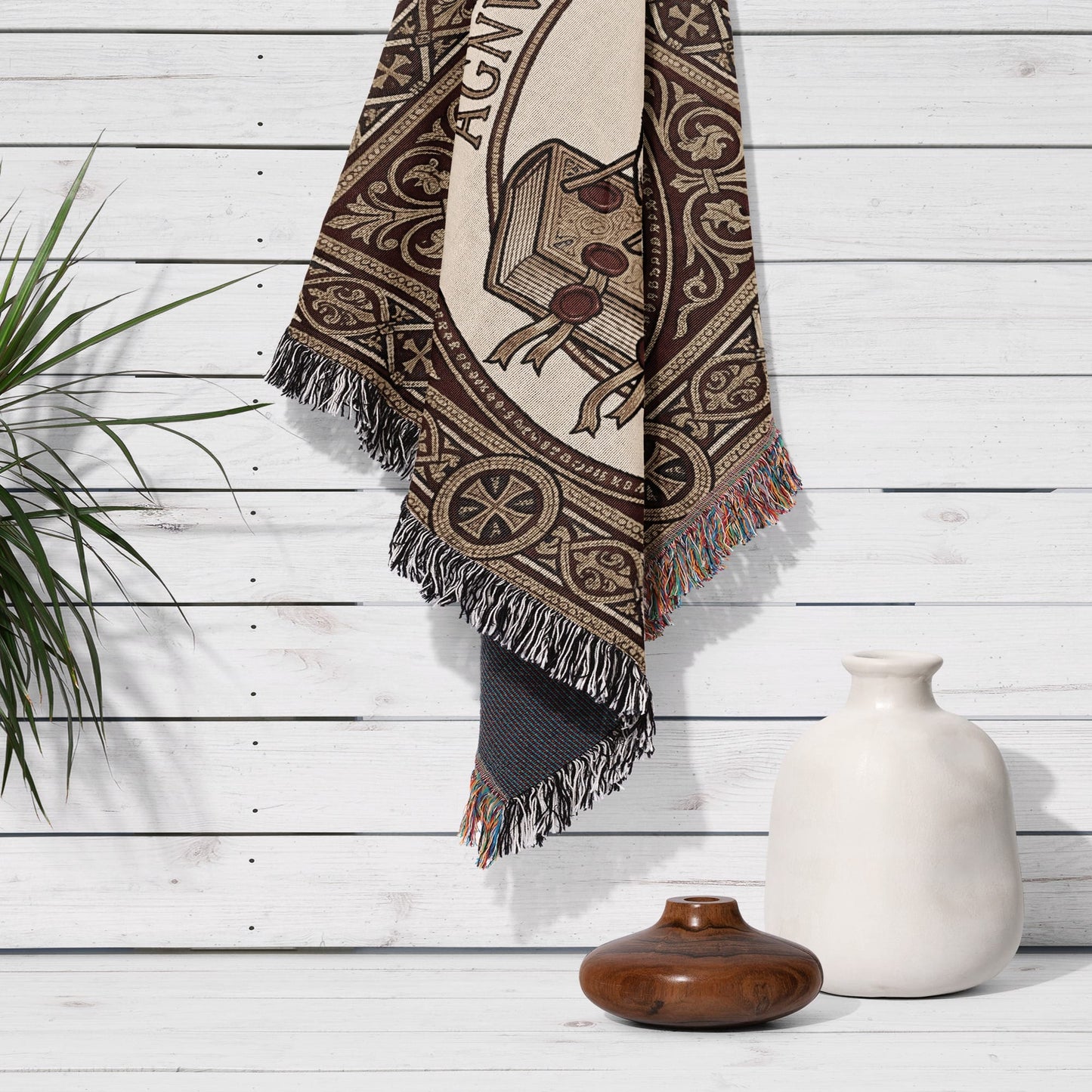 Tapestry with "AGNI" text hanging on a white wood-paneled wall with vase.