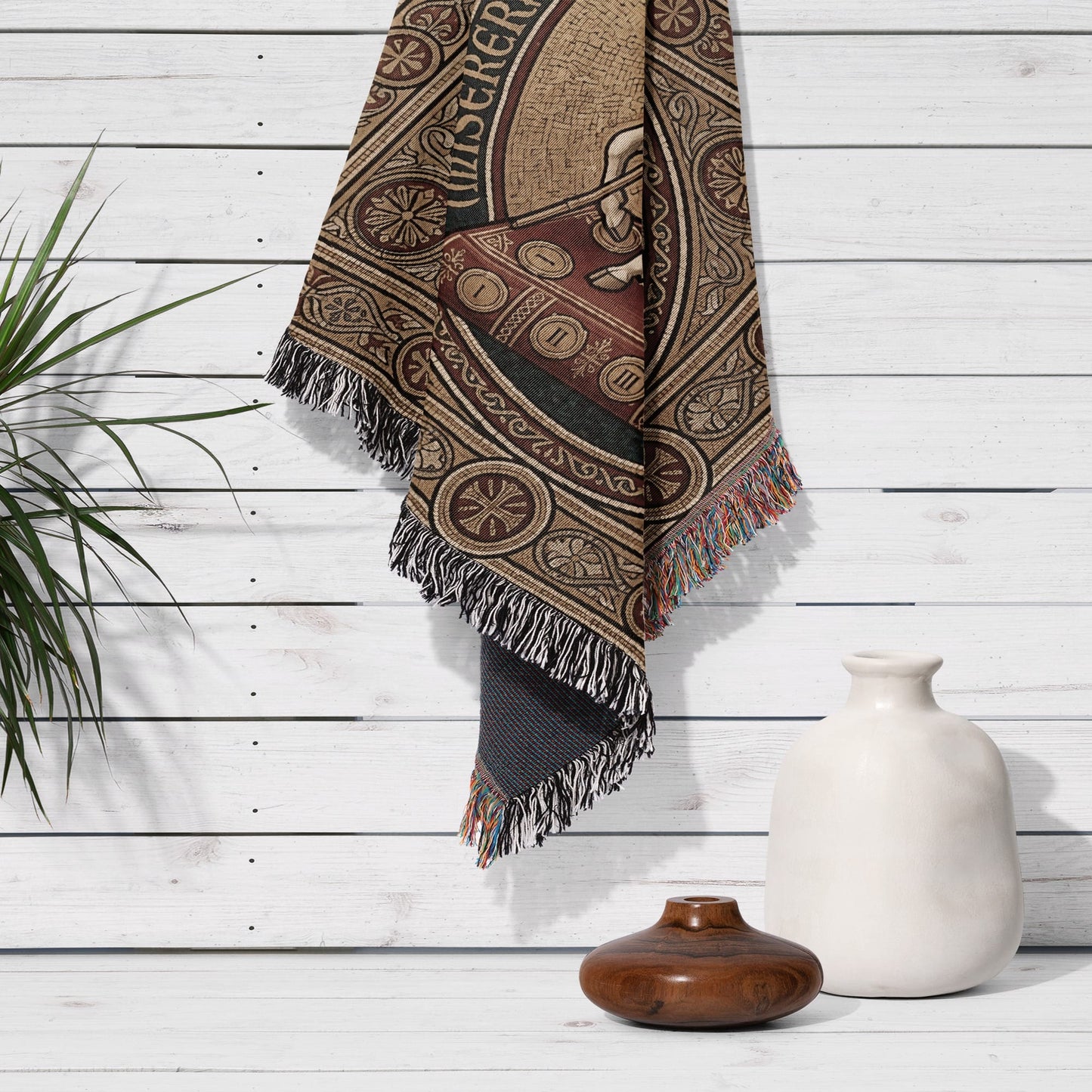 Woven blanket with intricate circular pattern and tassels, draped on white wall.