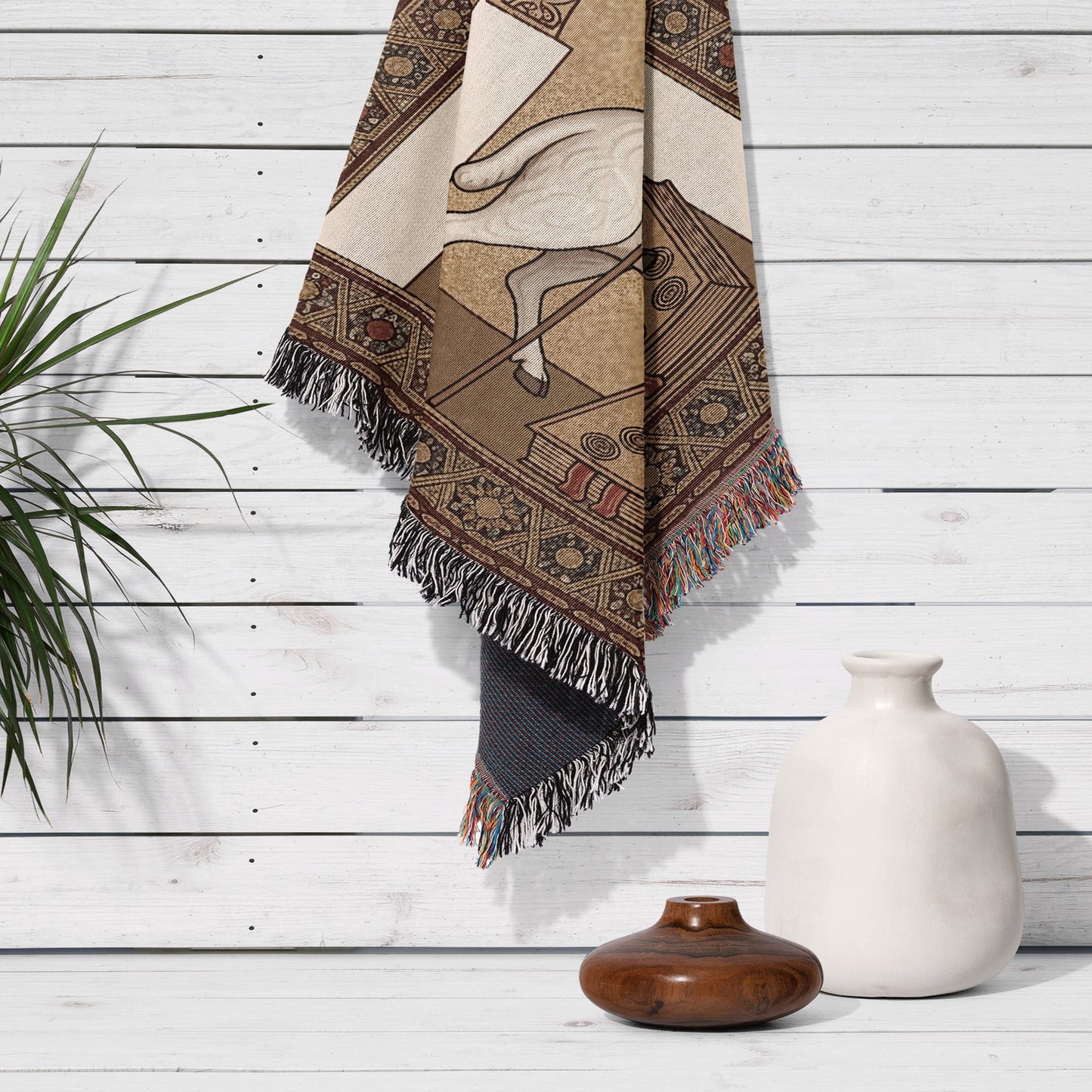 Woven blanket with geometric patterns and sheep motif hanging on a white wooden wall.