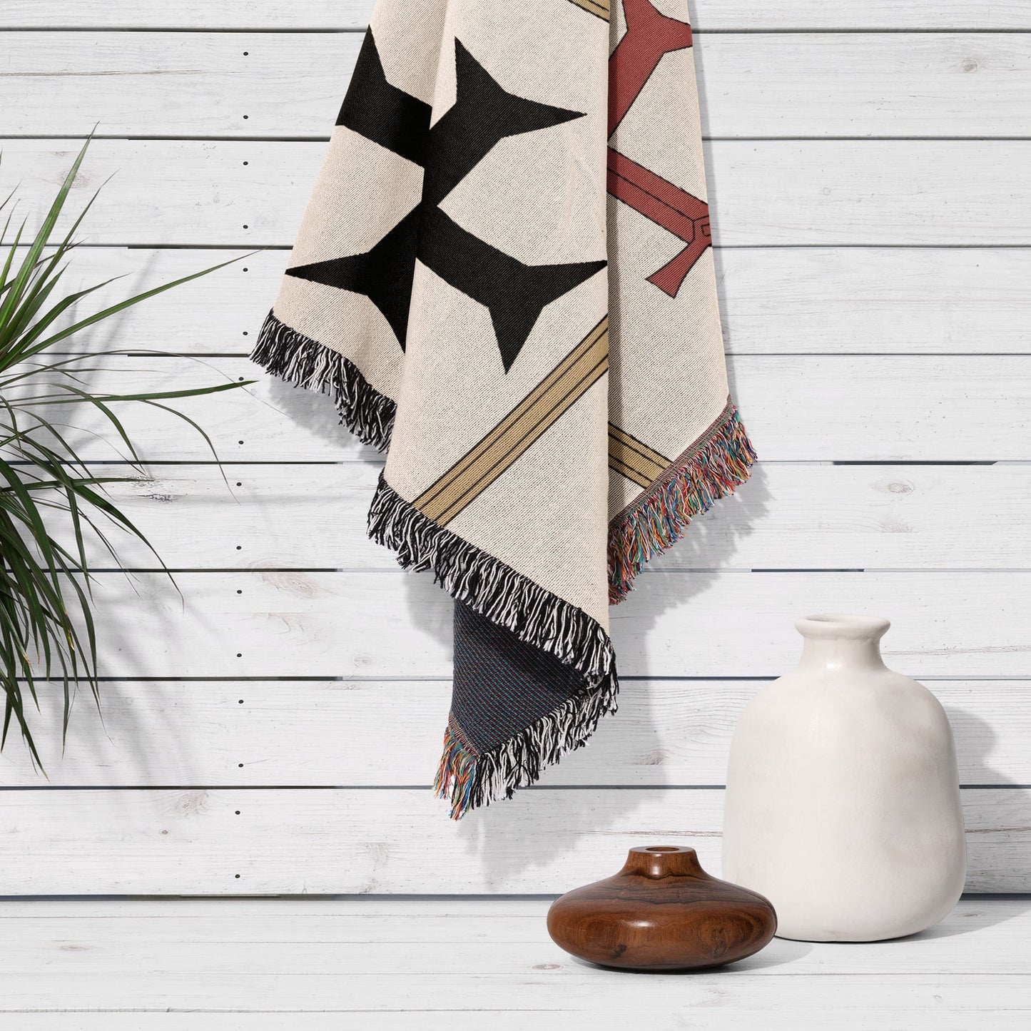 Textile blanket with geometric pattern and fringed edges draped over a white wooden wall.