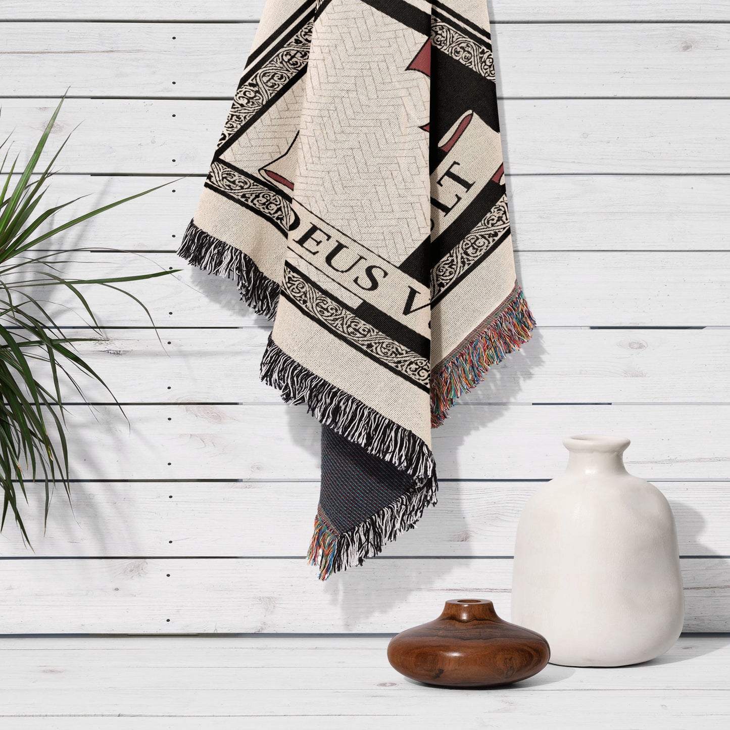 Woven throw blanket with "Deus Vult" text hanging on white wood paneling.