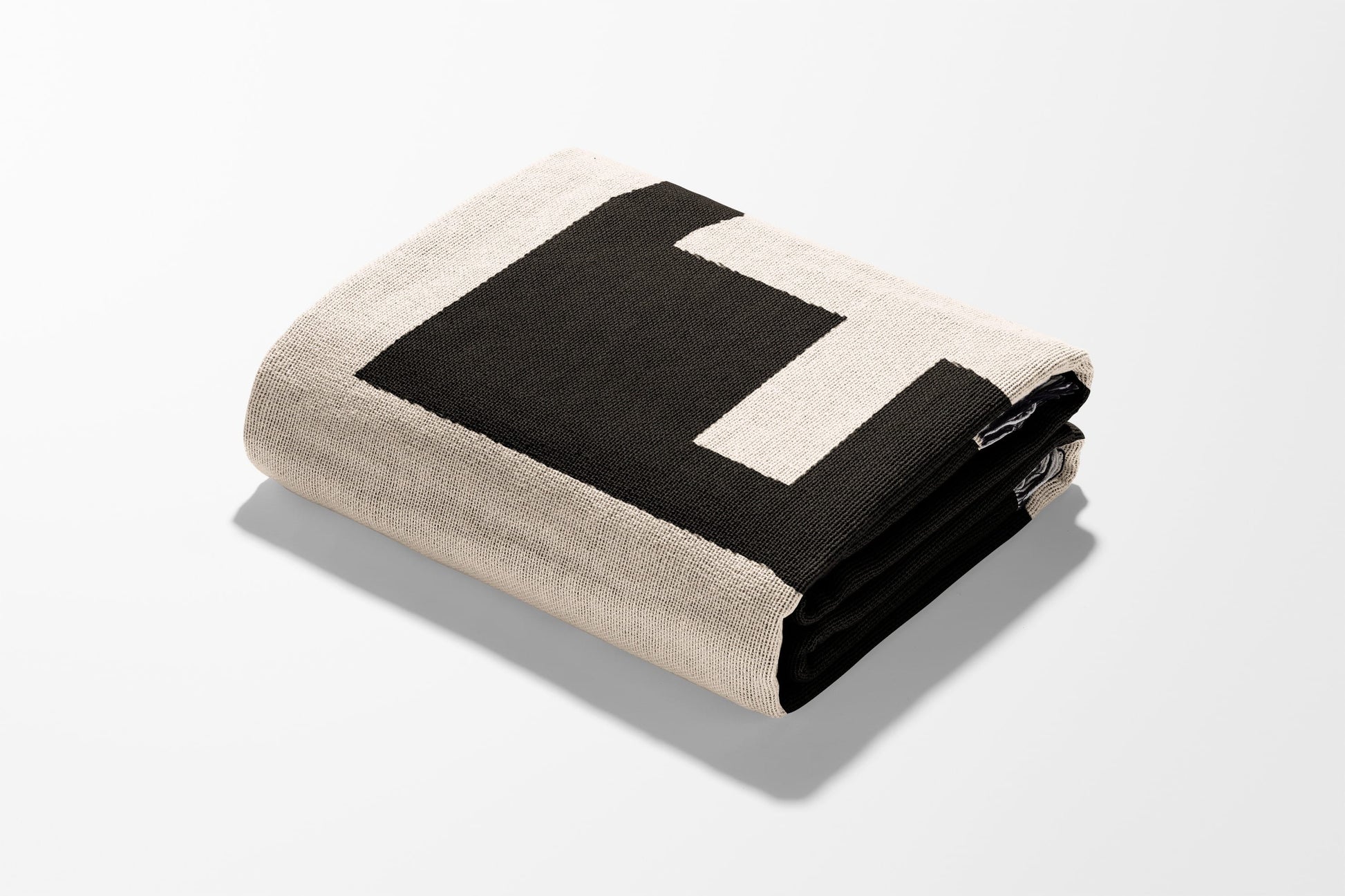 Cream and black striped knit throw blanket folded with shadow.