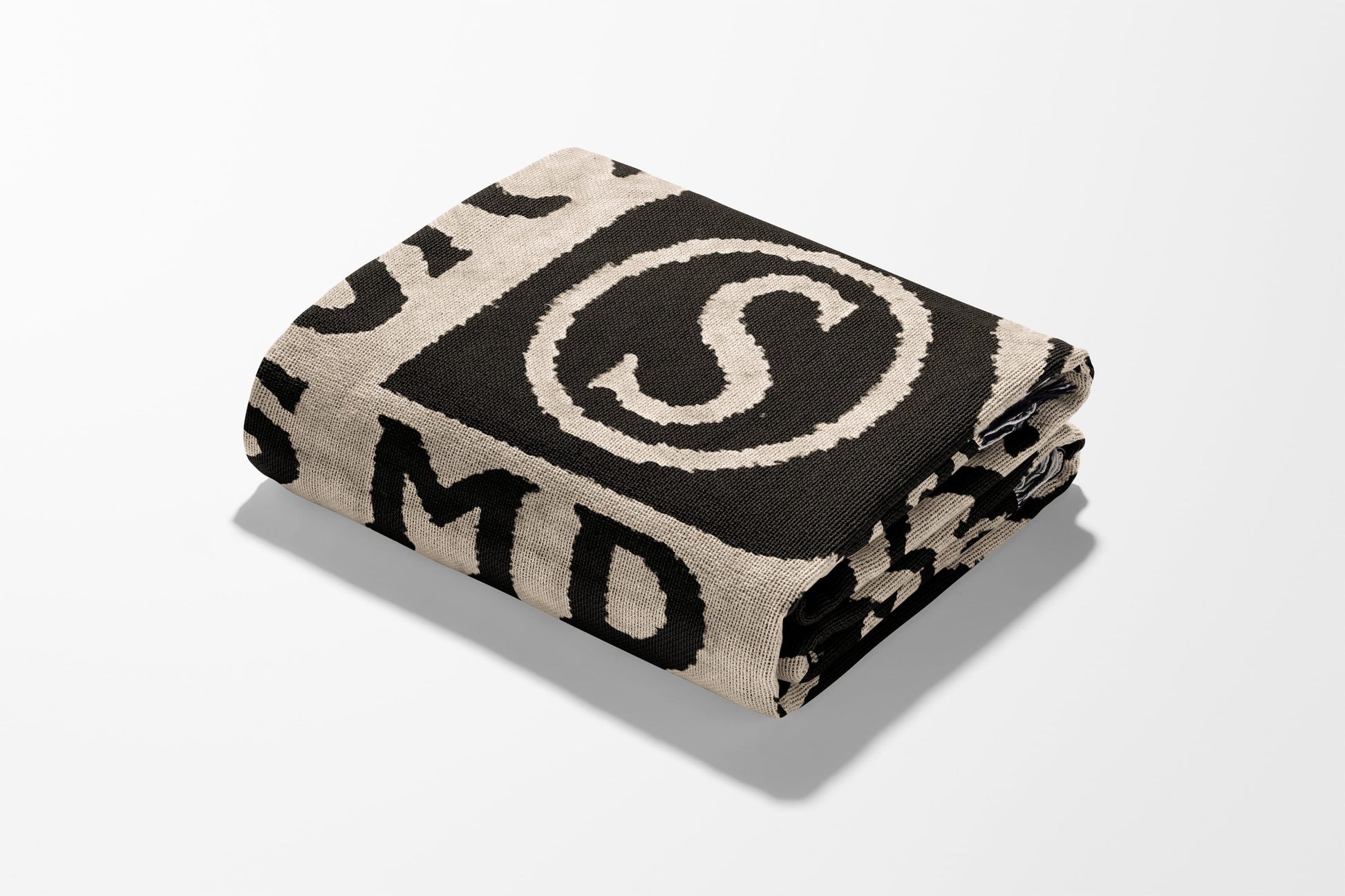Folded black and cream blanket with large 'S' and letters.