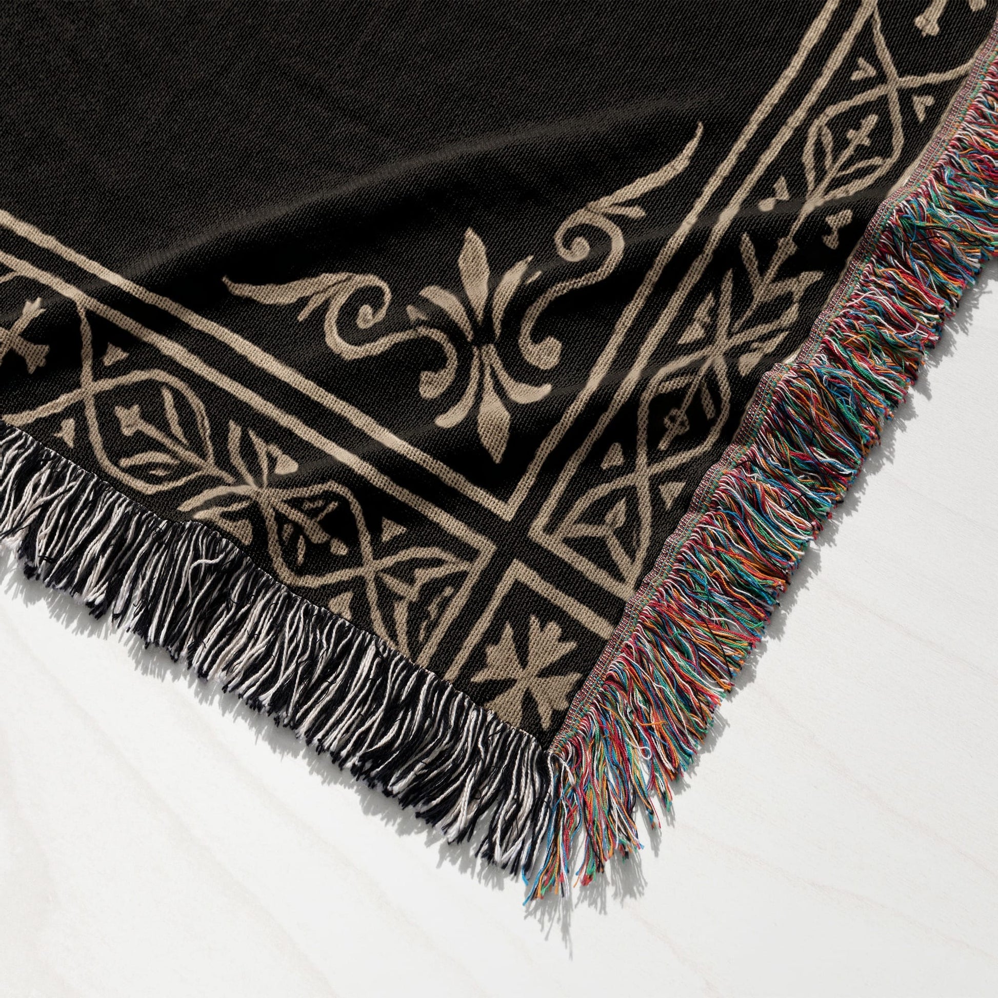 Black throw blanket with intricate cream pattern and colorful fringe.