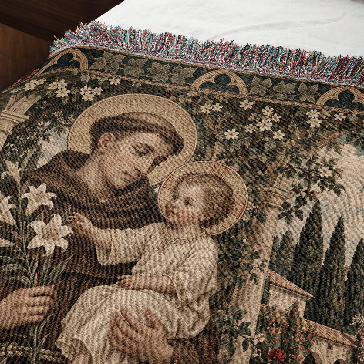 Woven tapestry throw blanket featuring Saint Anthony holding the Christ Child amidst white flowers and trees.