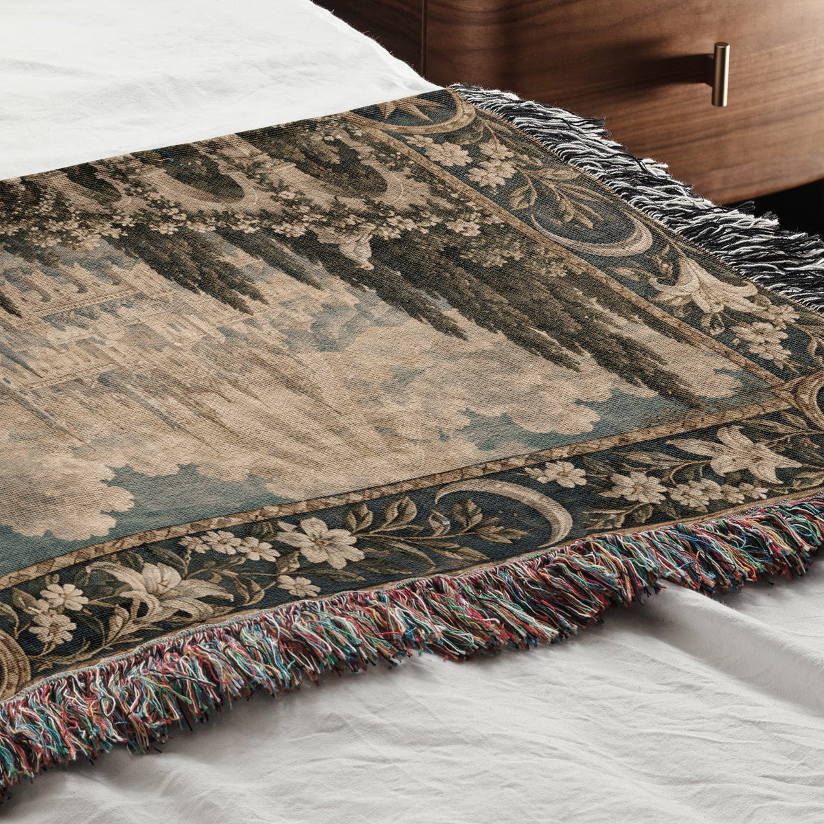 A woven tapestry throw blanket with a medieval landscape scene and a decorative floral border on a bed.