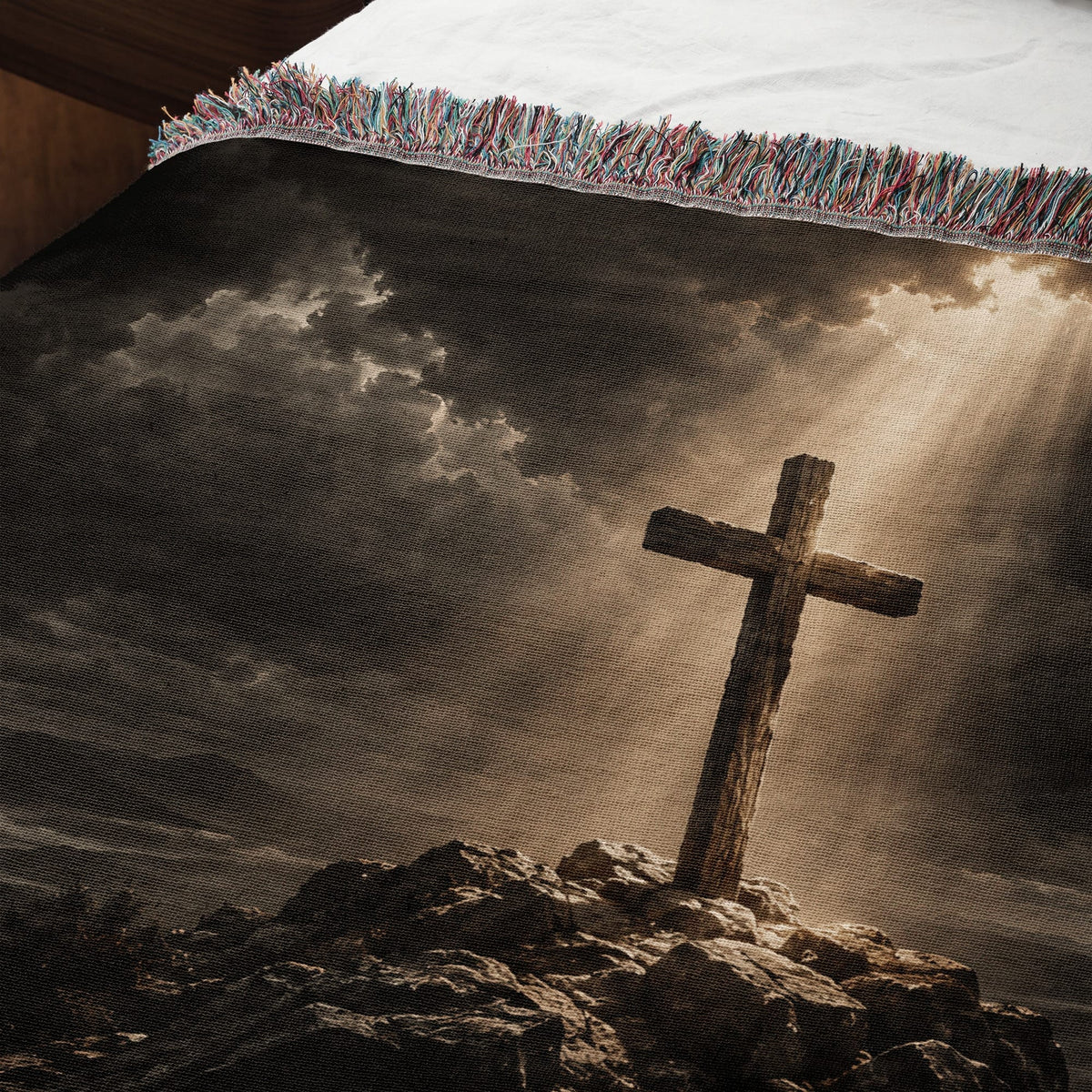 Woven throw blanket featuring a wooden cross atop a rocky hill under a cloudy, sunlit sky.