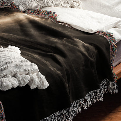 A dark brown woven throw blanket with multicolored fringed edges, draped over a bed.