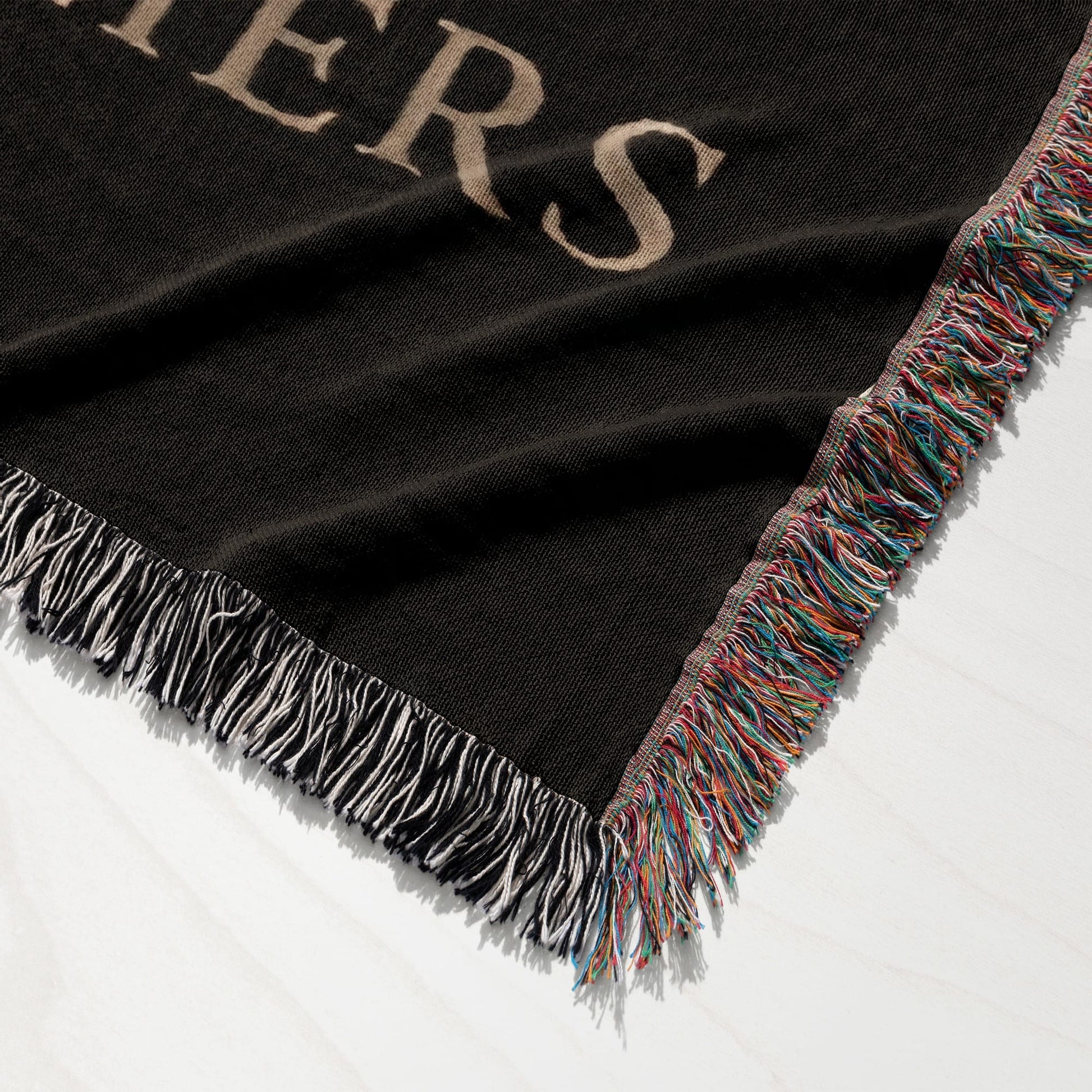 Black blanket with tan text and colorful frayed edges, laid on a white surface.