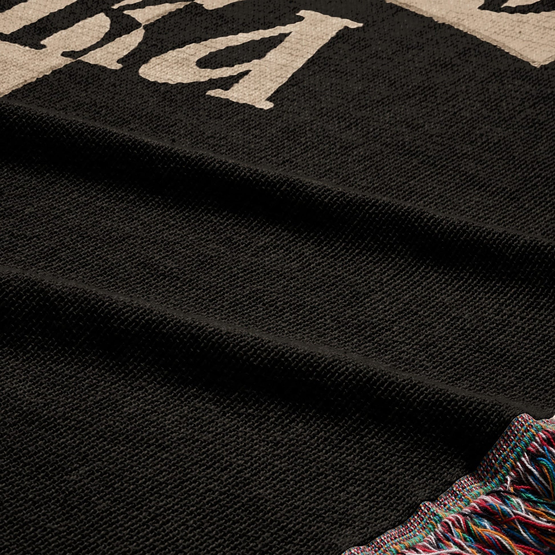 Black blanket with cream colored text and fringed edges.