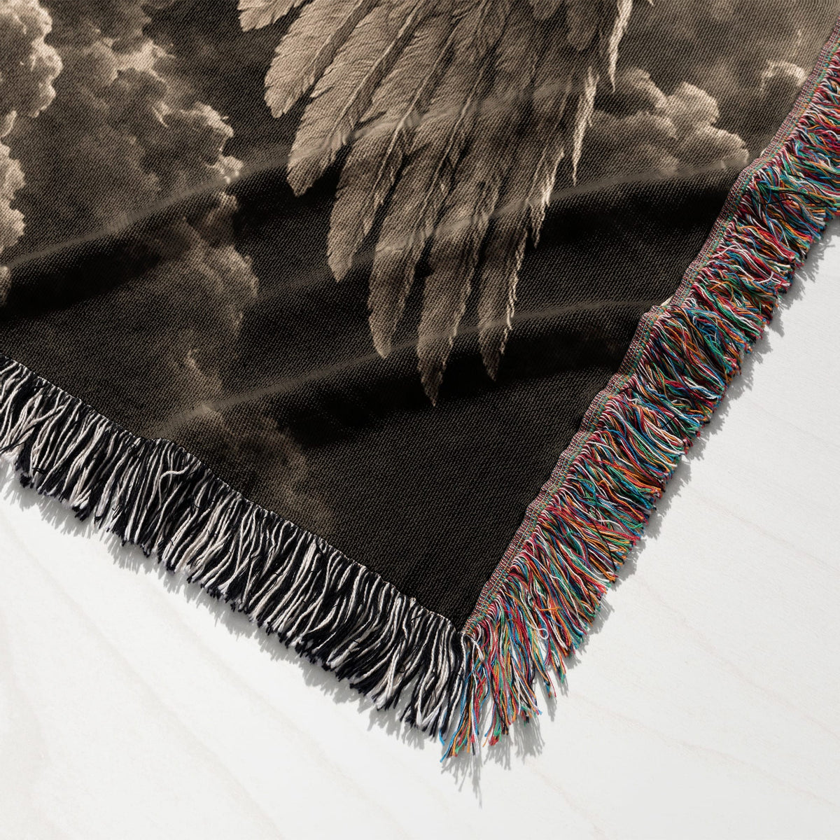 Woven throw blanket with fringed edges featuring a vintage black and white winged figure against cloudy skies.