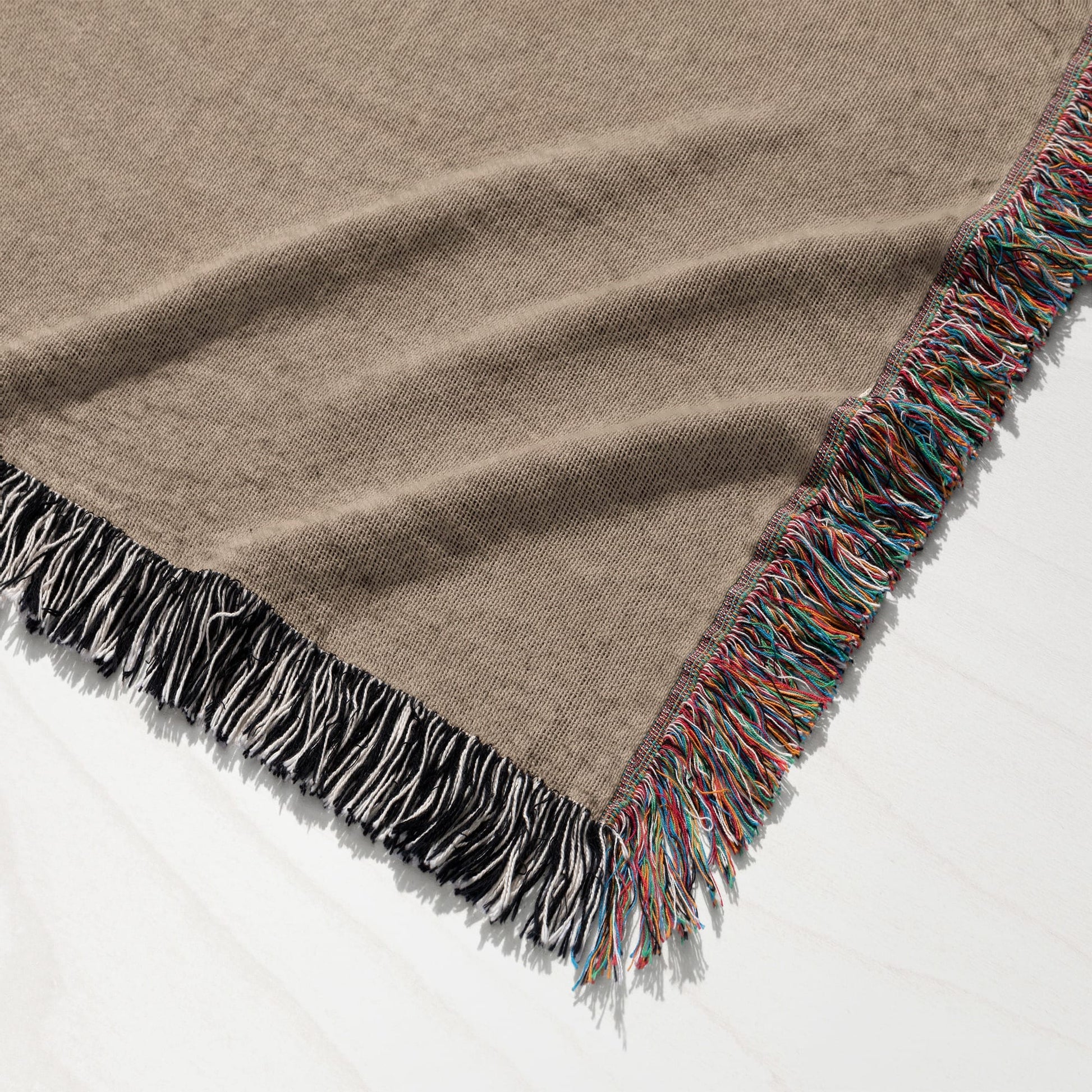 Tan woven blanket with multicolor and black/white fringe edges.