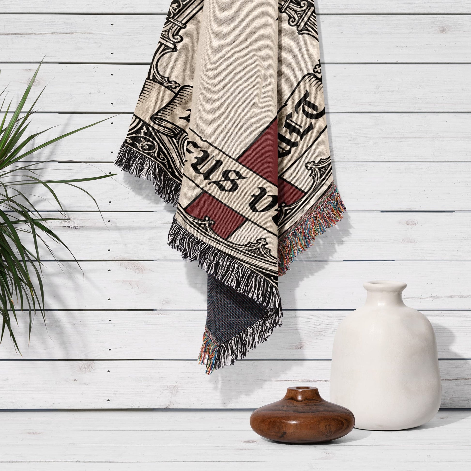 Textile art with fringe on white wooden wall, featuring large text.