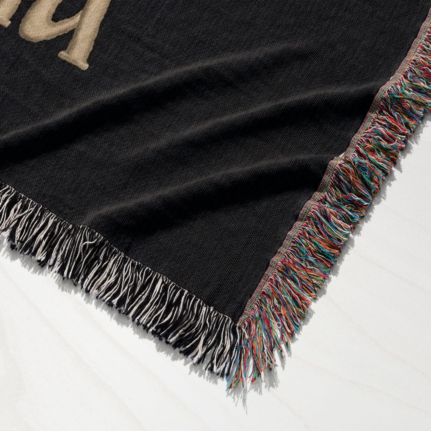 Black woven throw blanket with fringed edges and gold lettering.