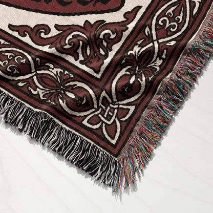 Woven tapestry blanket with ornate scrollwork and fringed edges on a white surface.