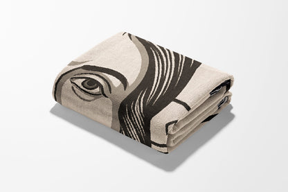 Folded blanket with abstract eye graphic design in beige and black.