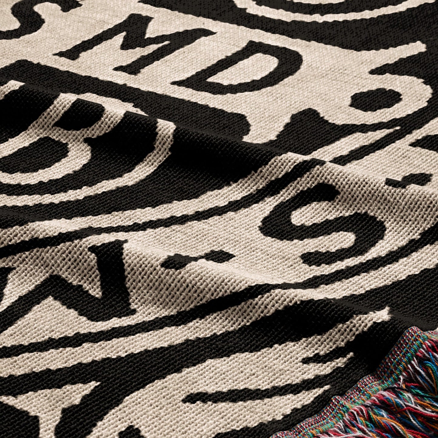 Woven blanket with black and cream pattern and colorful fringe.
