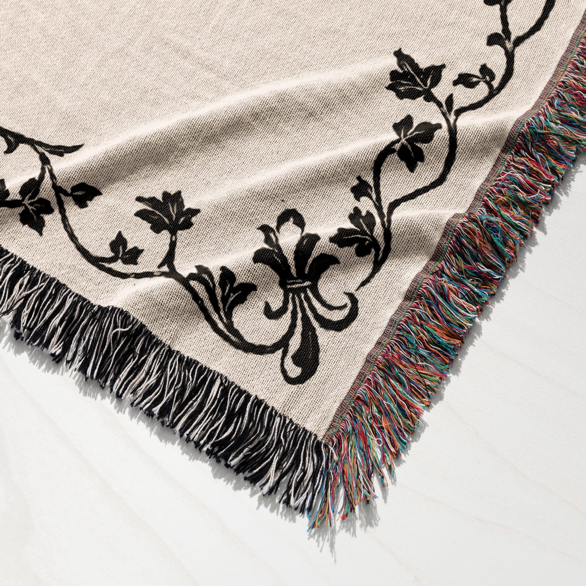 Beige throw blanket with black floral pattern and multicolored fringe.