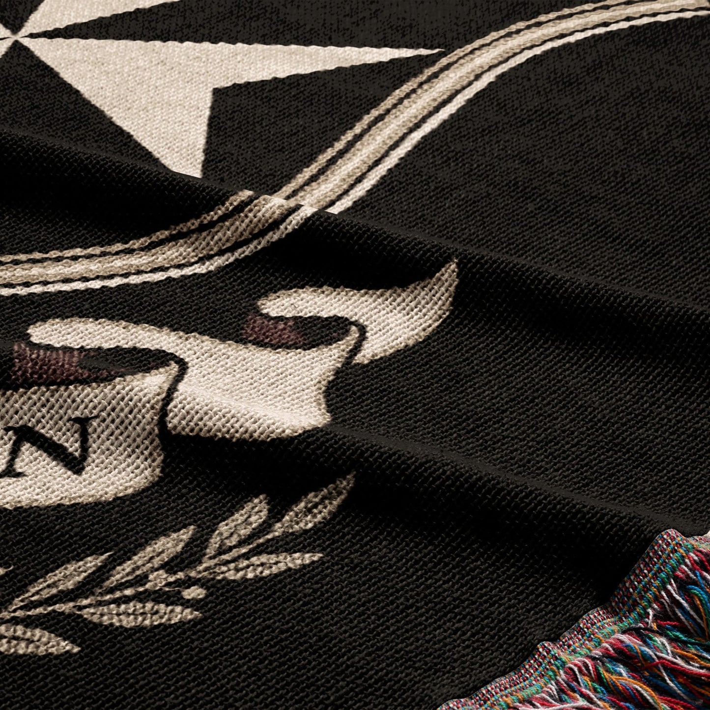 Black woven blanket with a white star, scroll, and fringe detail.