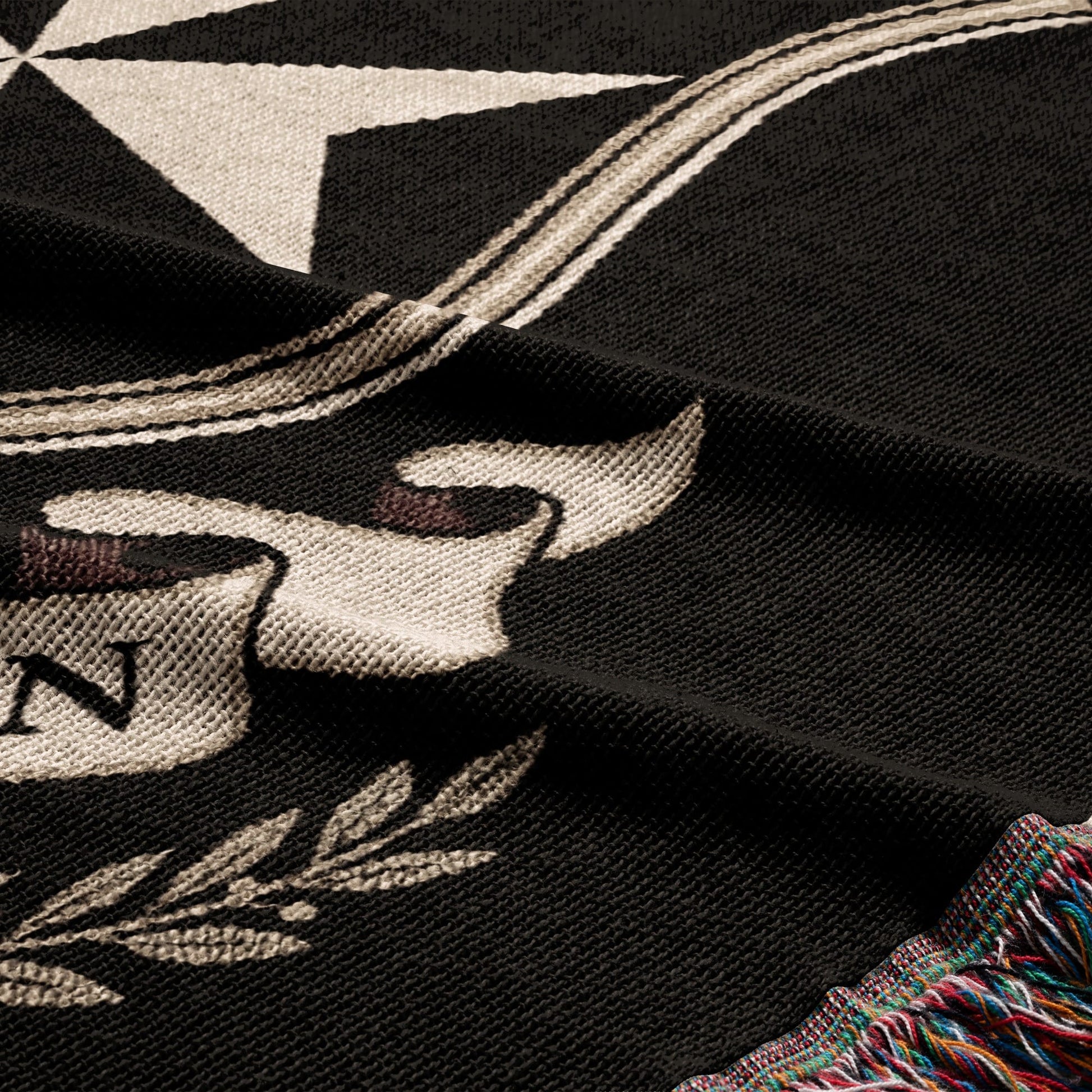 Black woven blanket with a white star, scroll, and fringe detail.