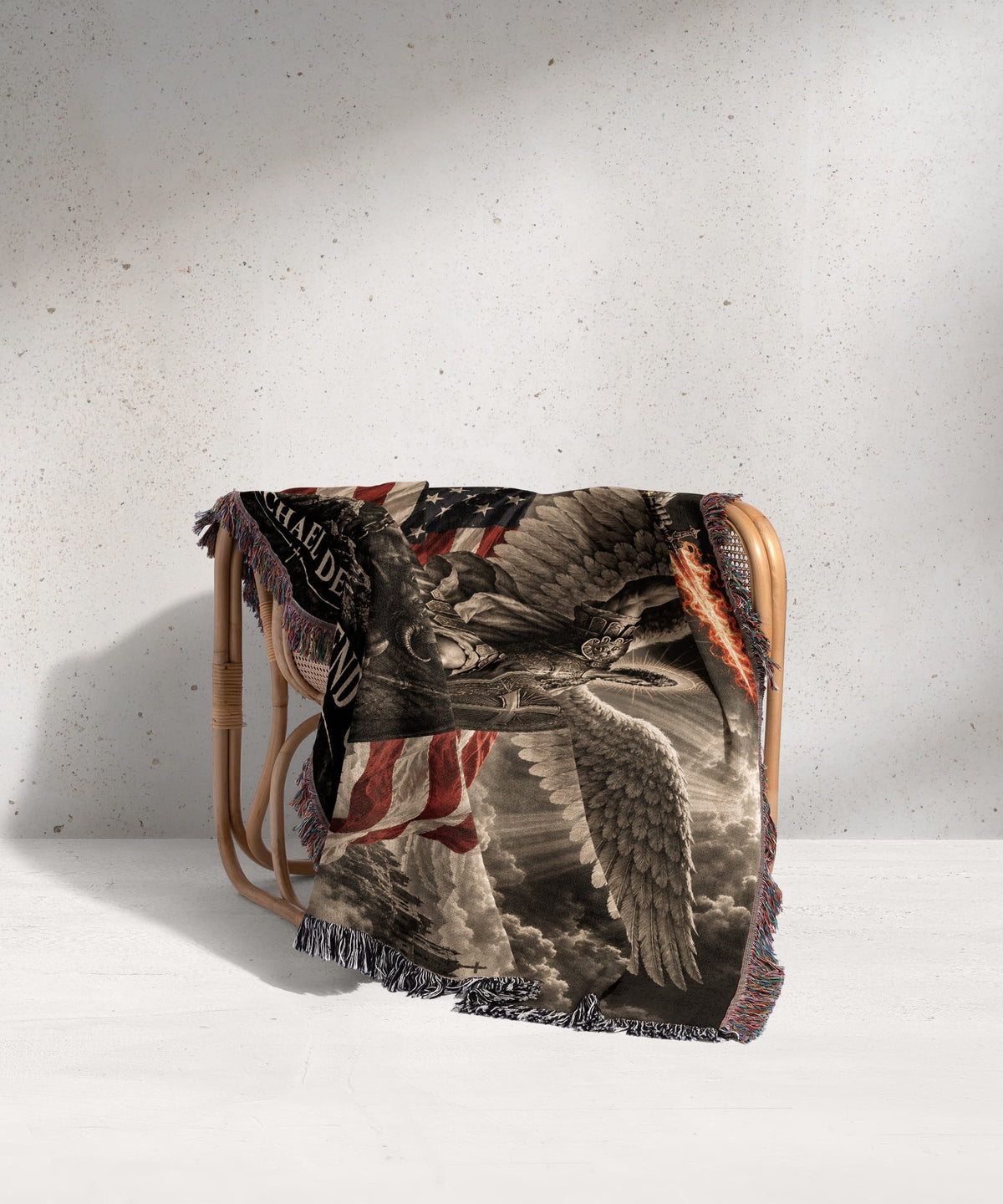 A woven blanket featuring a winged angel, an American flag, and text draped over a rattan chair.