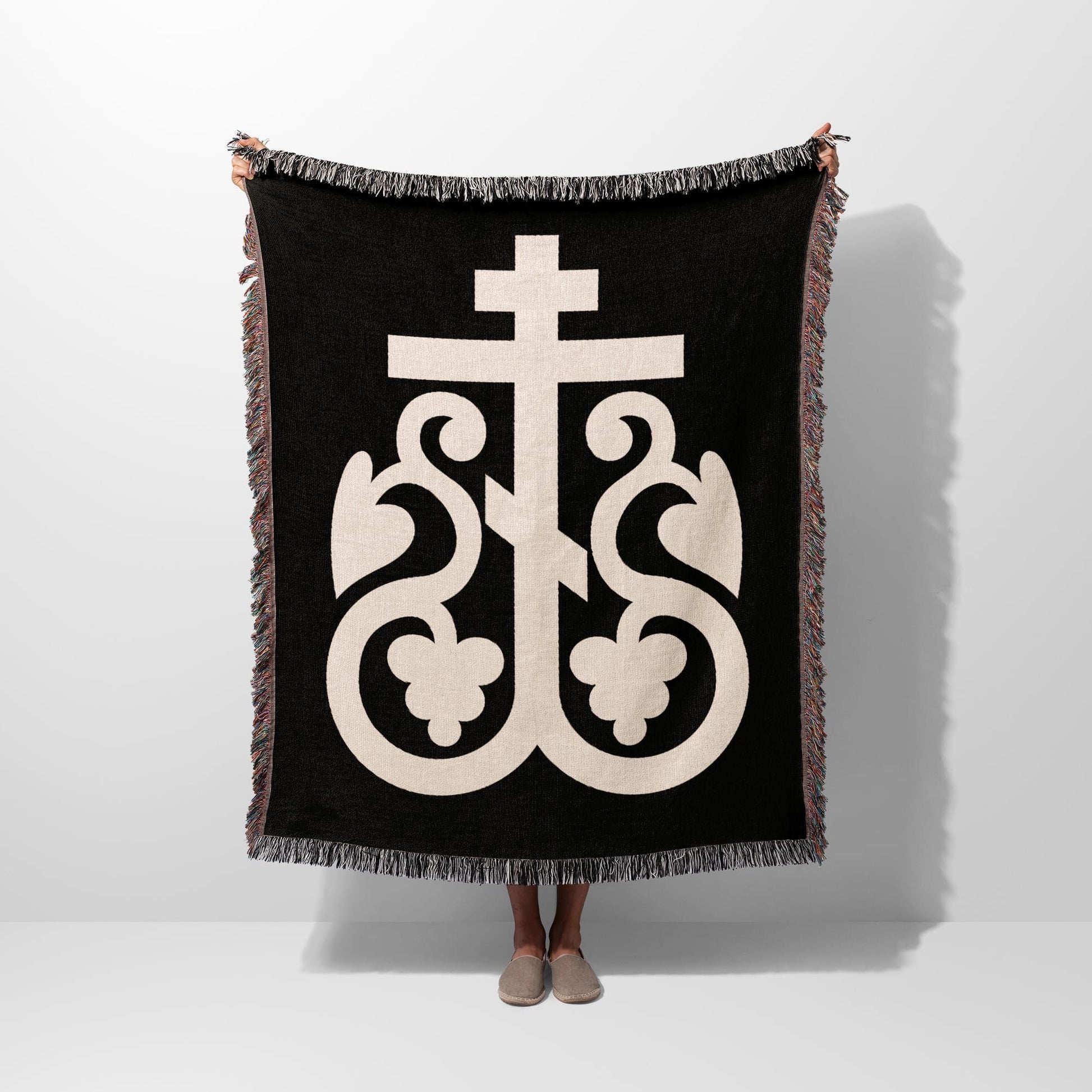 Black woven blanket with large cream-colored ornate cross symbol and fringed edges.