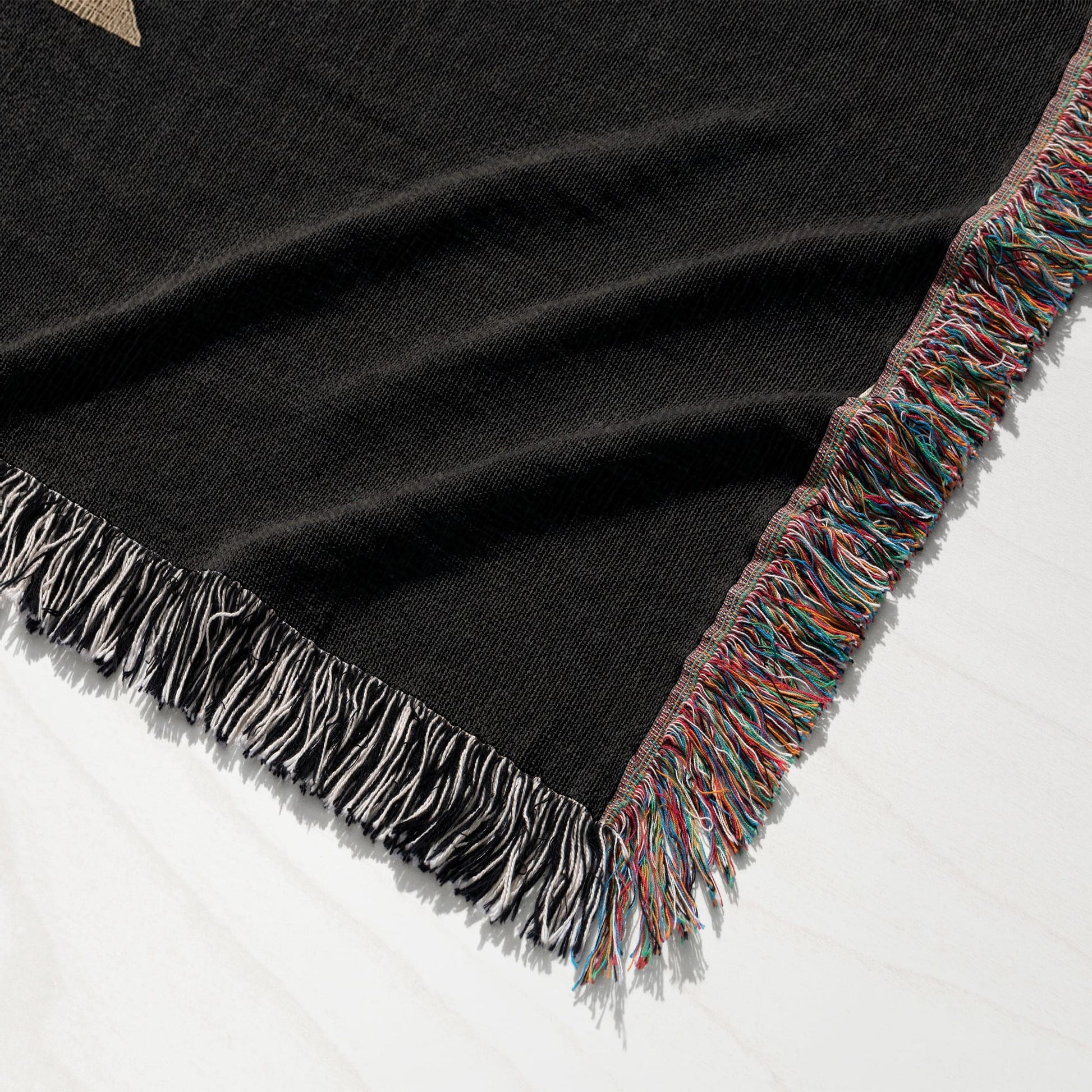 Black woven blanket with multicolored fringe on white surface.