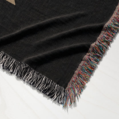 Black woven blanket with multicolored fringe on white surface.