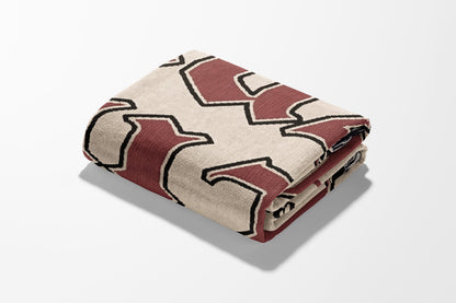 Folded tan blanket with a dark red geometric pattern.