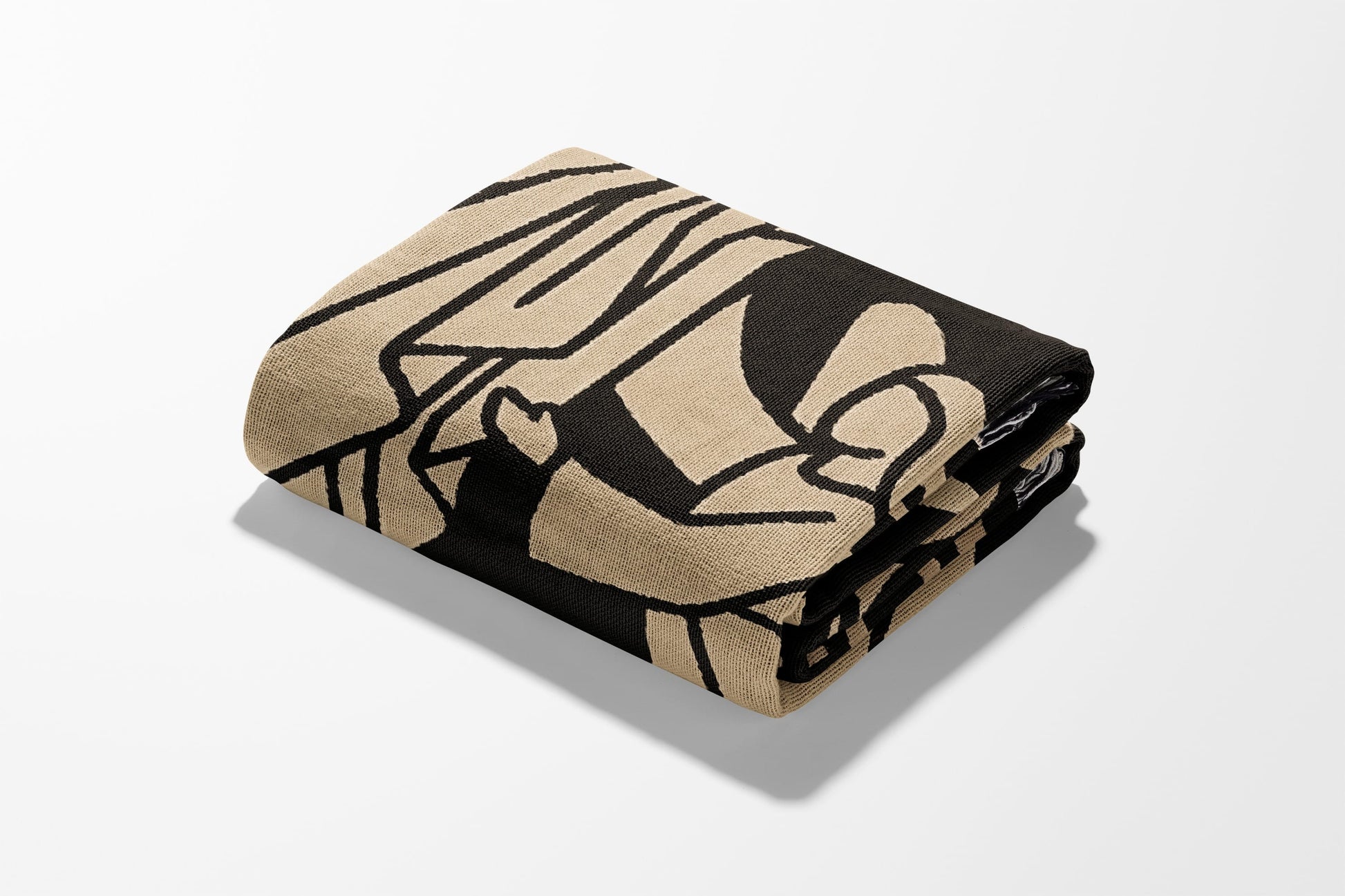 Folded beige and black patterned throw blanket on a white surface.