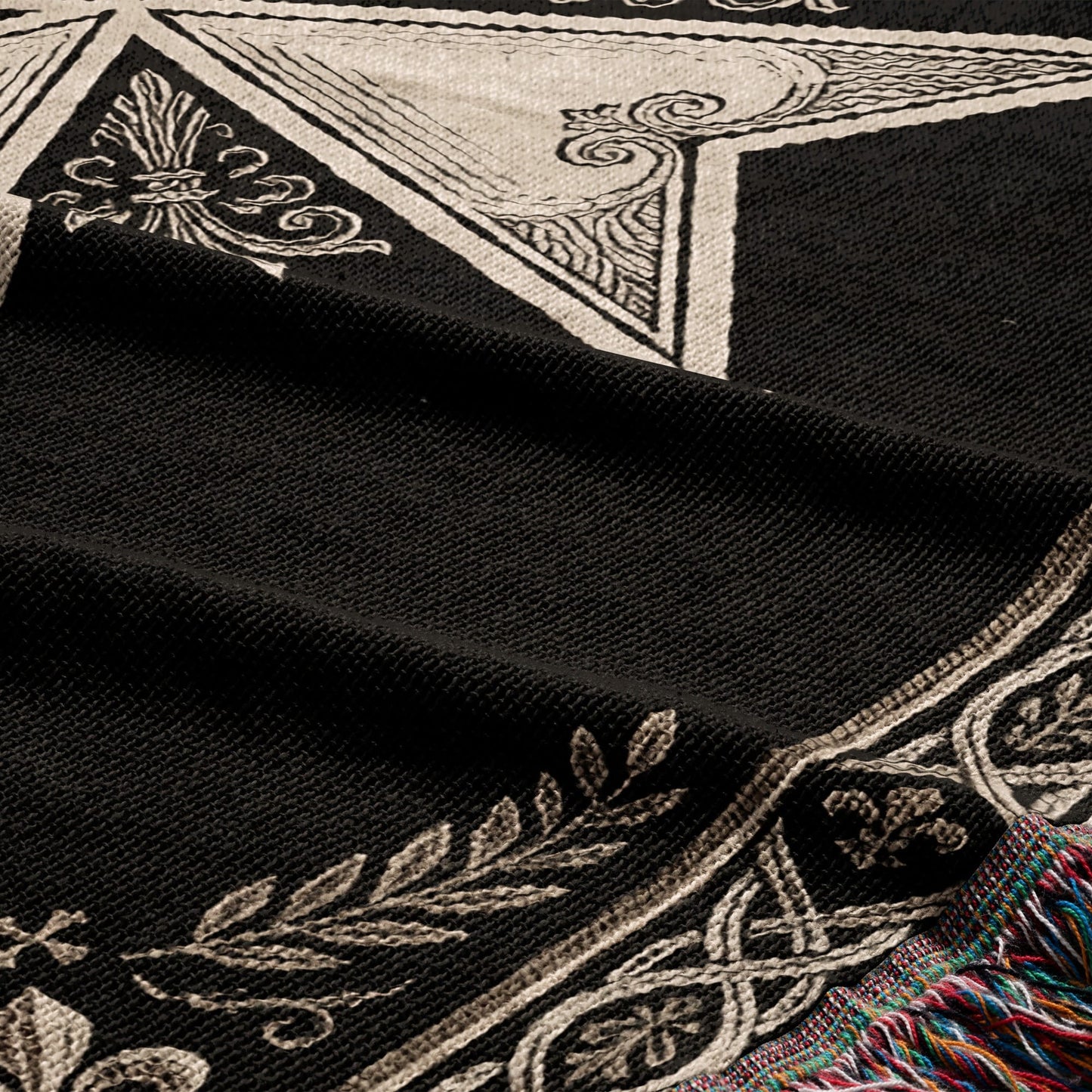 Black woven blanket with white ornate design and a fringed edge.