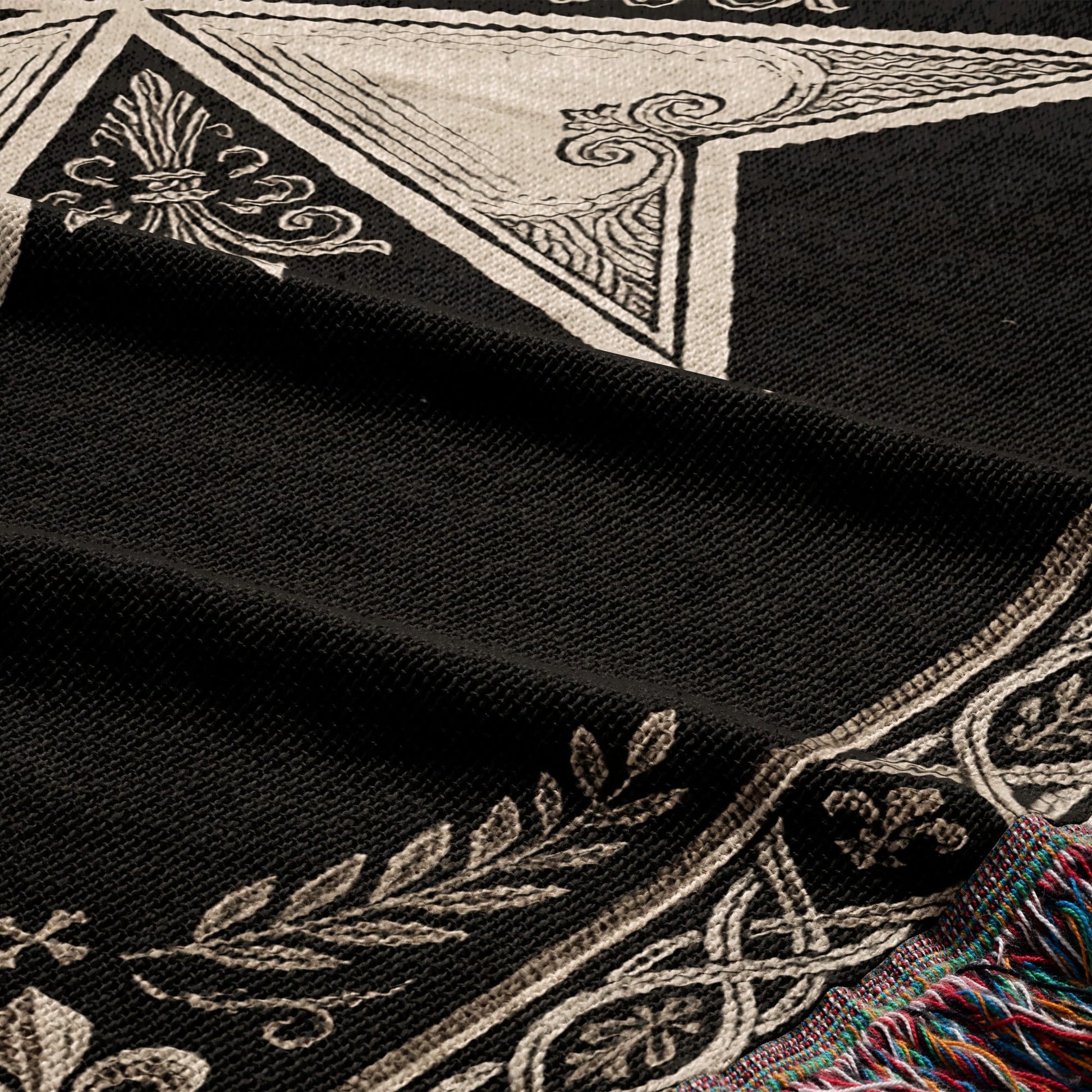 Black woven blanket with white ornate design and a fringed edge.