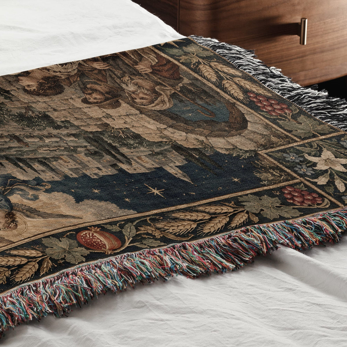 A woven medieval tapestry blanket with a castle scene and fringe border draped across a white bed.