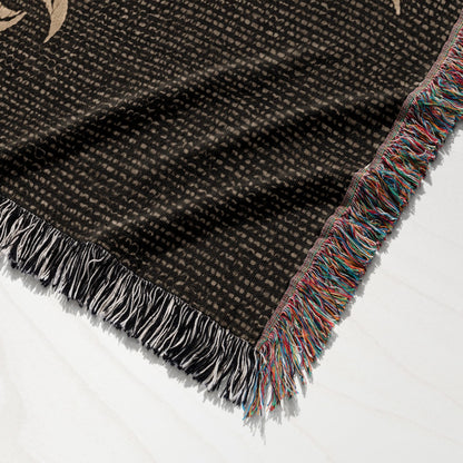Black woven blanket with colorful fringed edges on a white surface.
