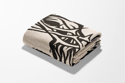 Folded blanket with black abstract design on cream background.