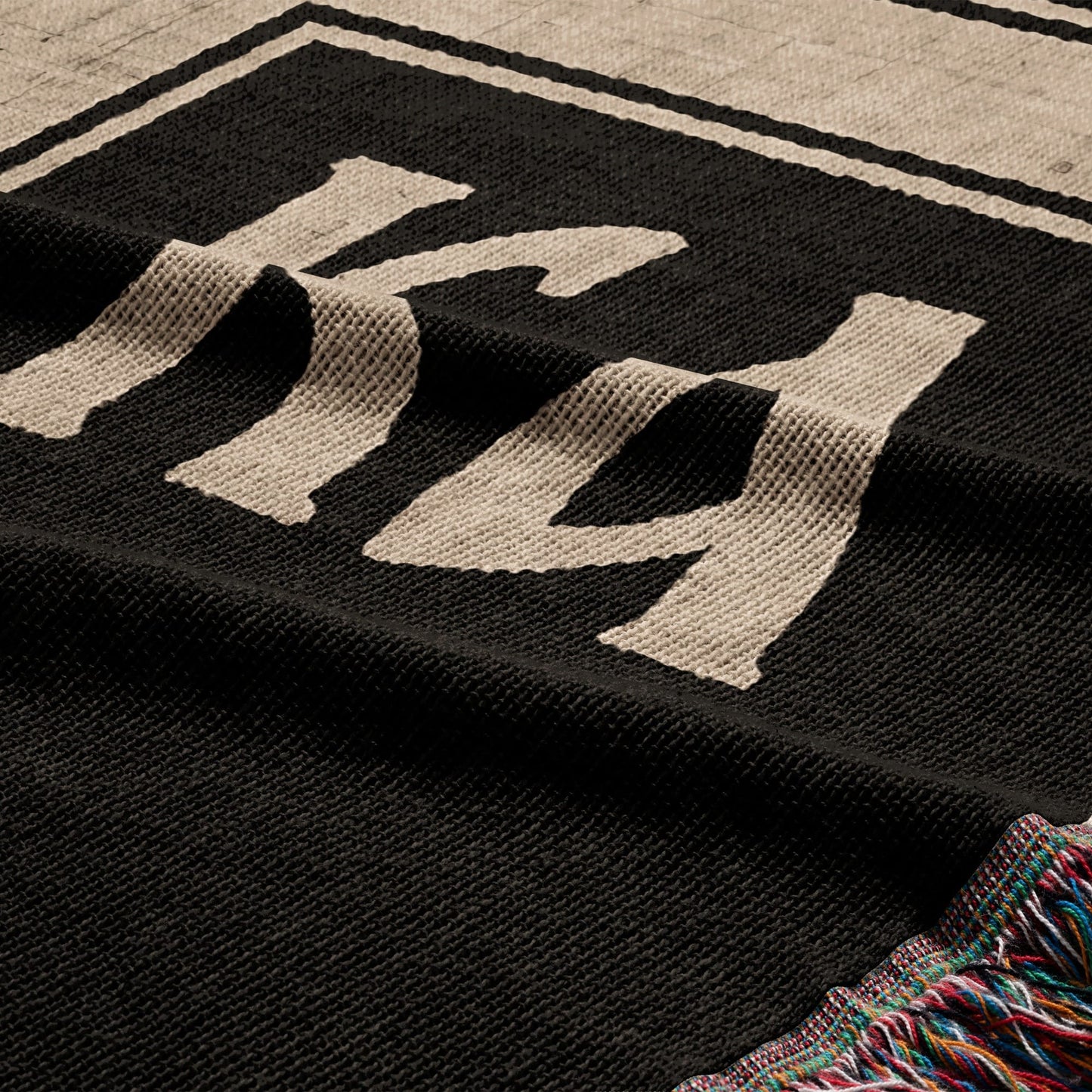 Black throw blanket with "KK" embroidered in beige and tasseled edges.