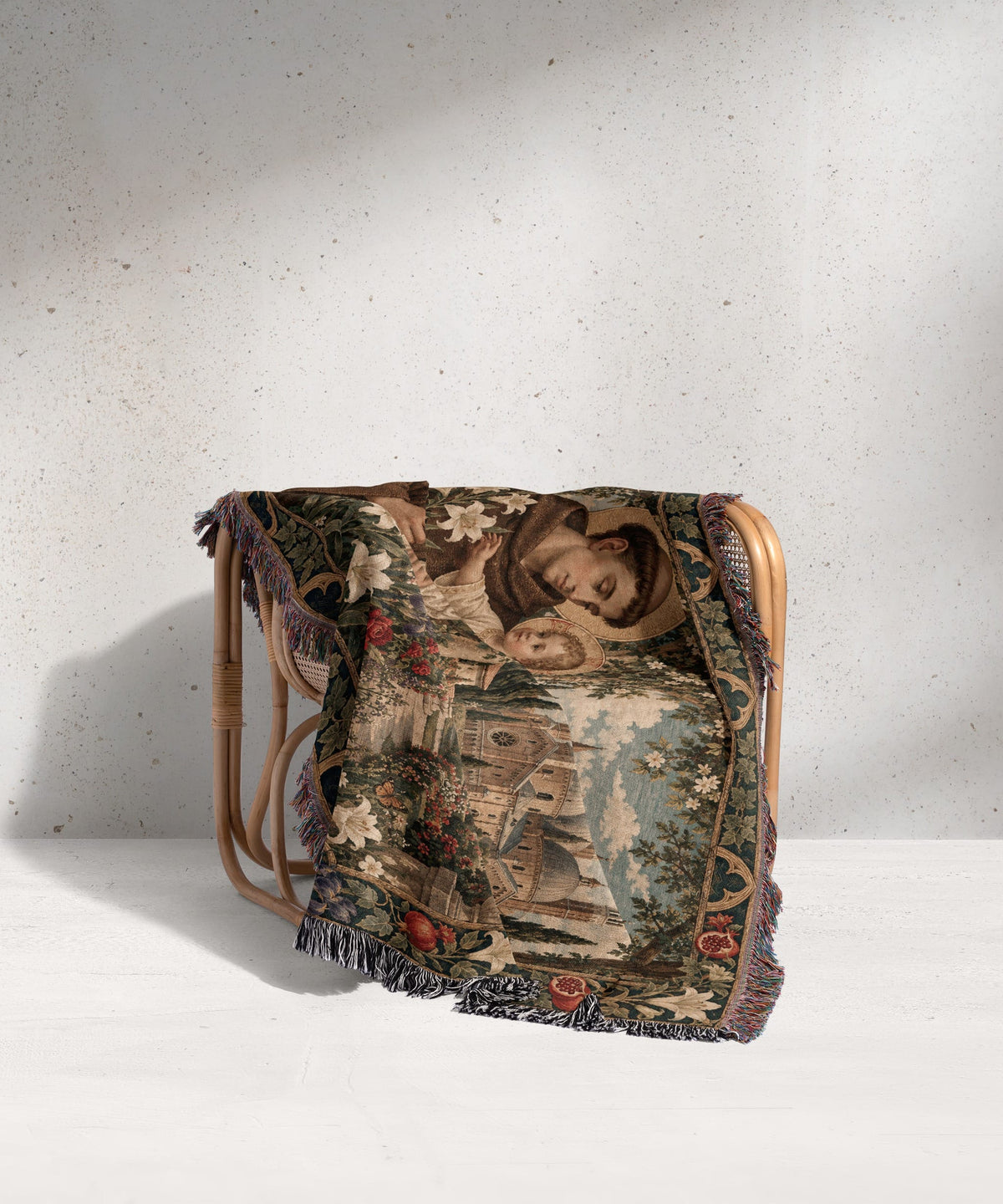 Woven throw blanket depicting a religious scene draped over a wicker chair against a grey wall.
