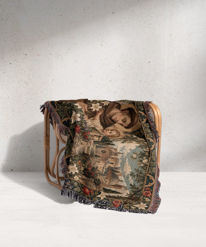 Woven throw blanket depicting a religious scene draped over a wicker chair against a grey wall.