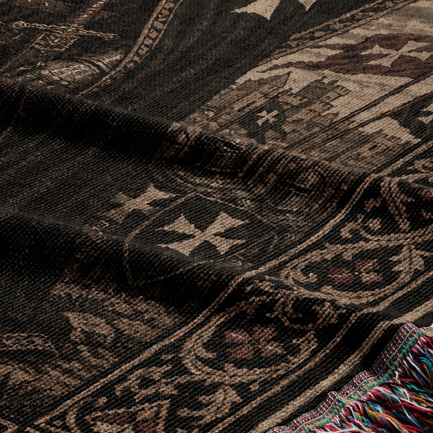 Dark woven fabric with ornate cross pattern and colorful fringed edge.