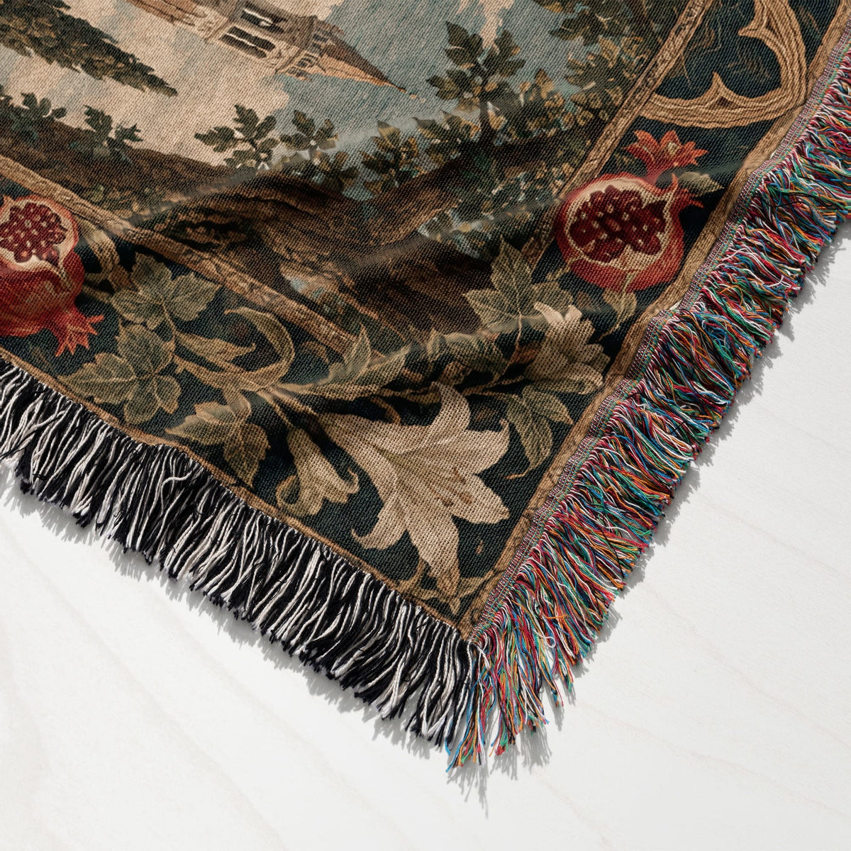 A woven blanket featuring a medieval landscape with a castle, trees, pomegranates, and multicolored fringe edging.