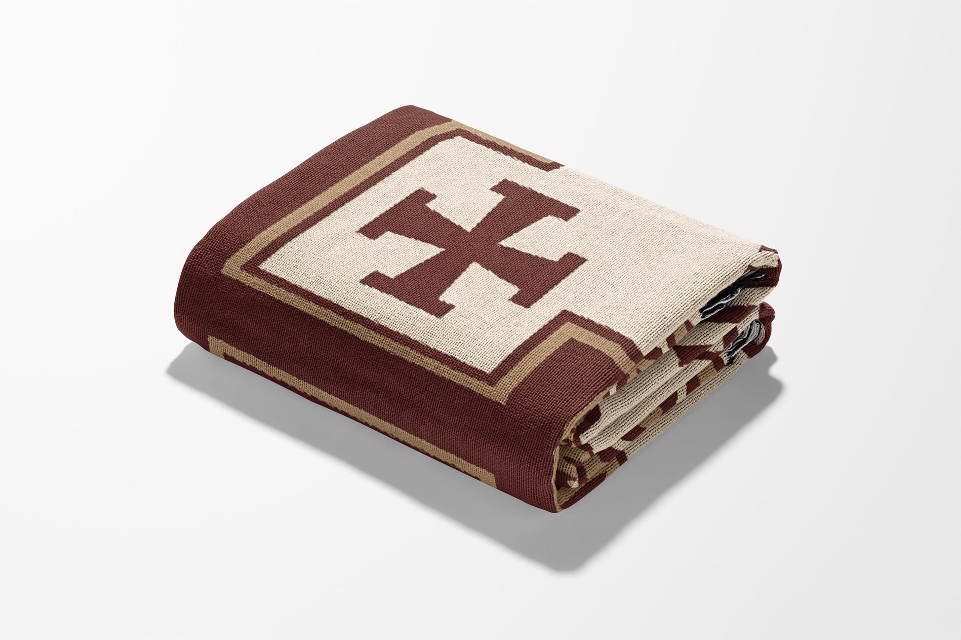 Folded blanket with a large taupe cross symbol on a maroon background.