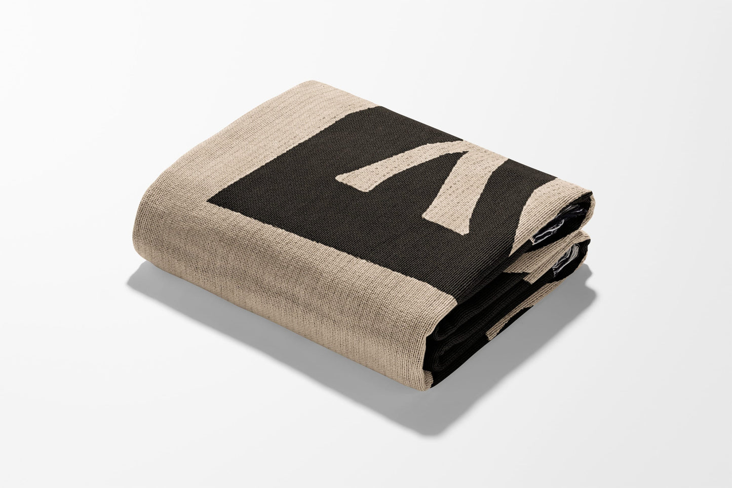 Folded beige blanket with a black "K" logo pattern.