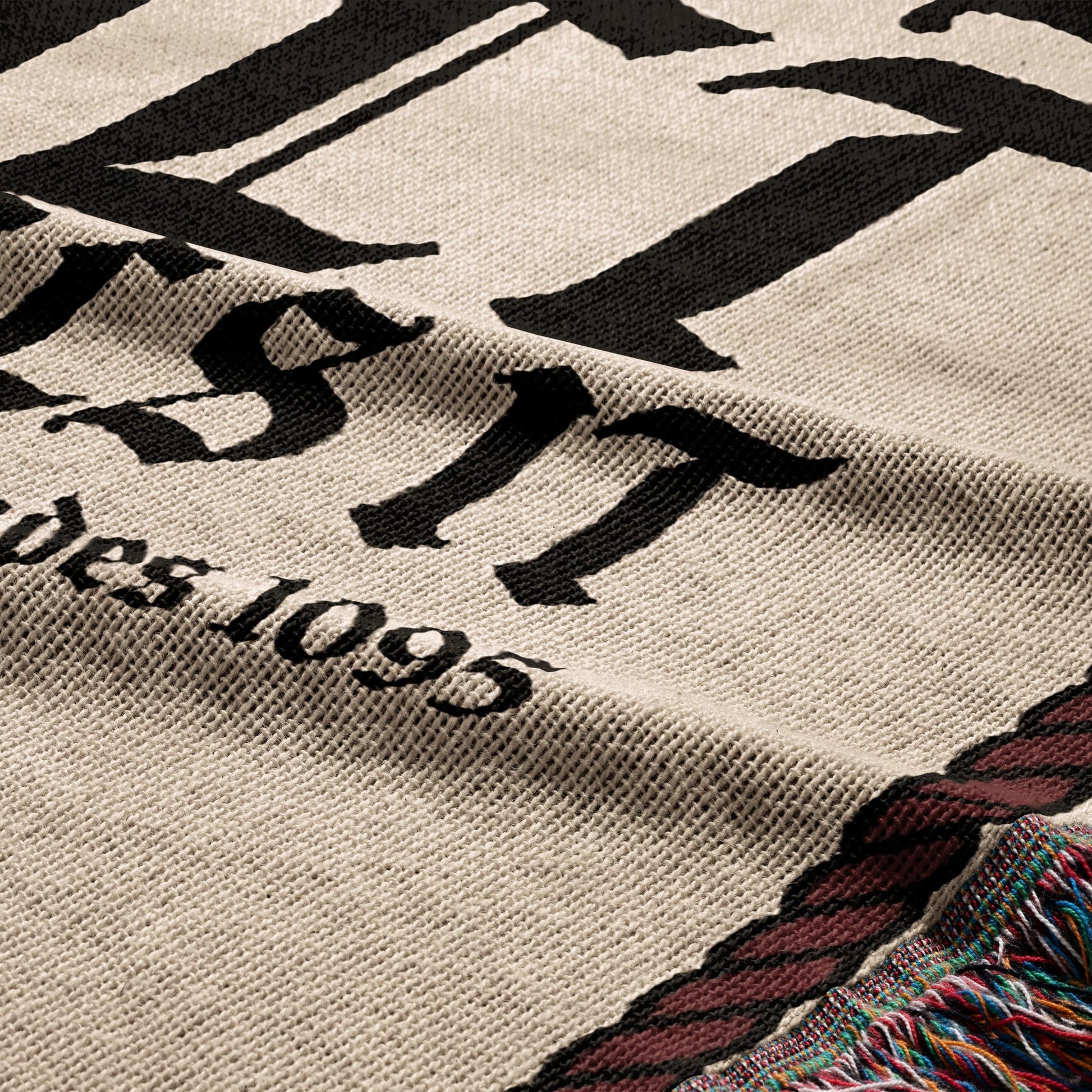 Tapestry with "EST. 1895" text and tasseled edge.