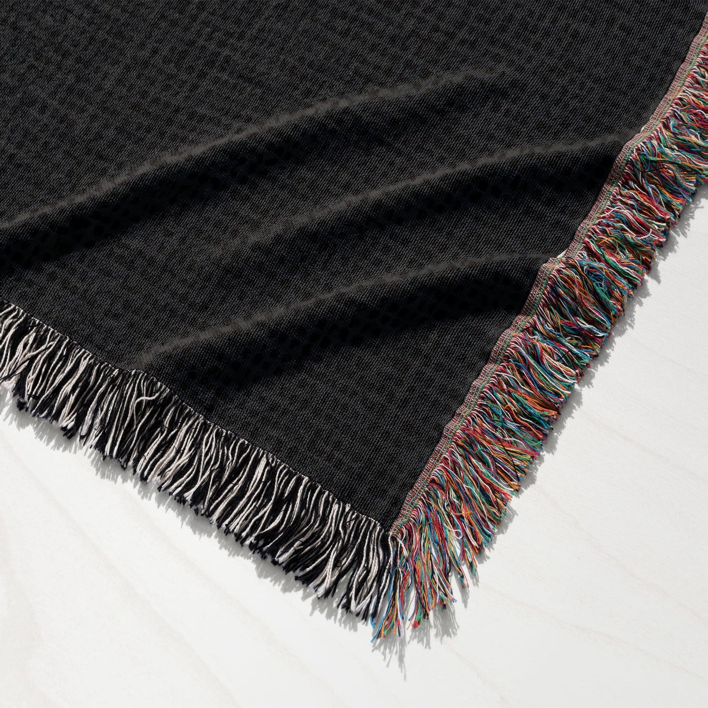 Black woven throw blanket with colorful fringed edges.