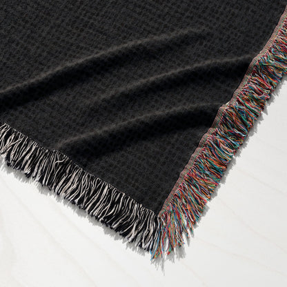 Black woven throw blanket with colorful fringed edges.