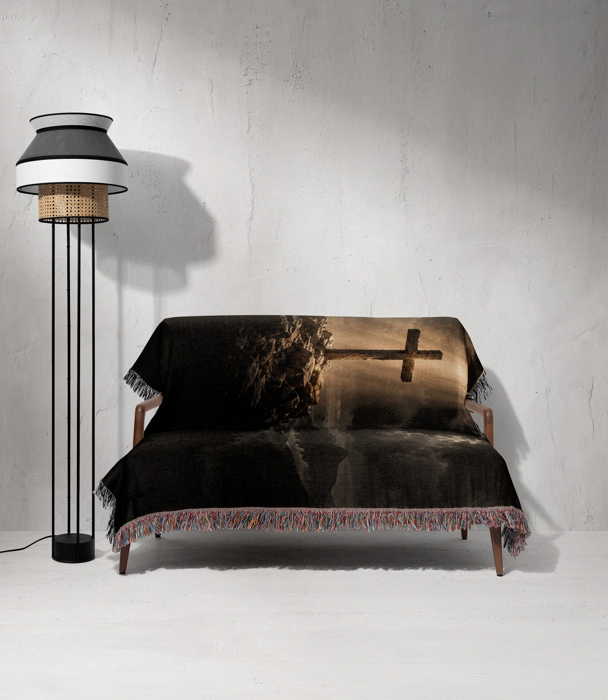 A patterned throw blanket with a fringed edge covers a small couch beside a modern floor lamp.