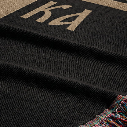 Black woven throw blanket with "KA" logo and colorful fringe.