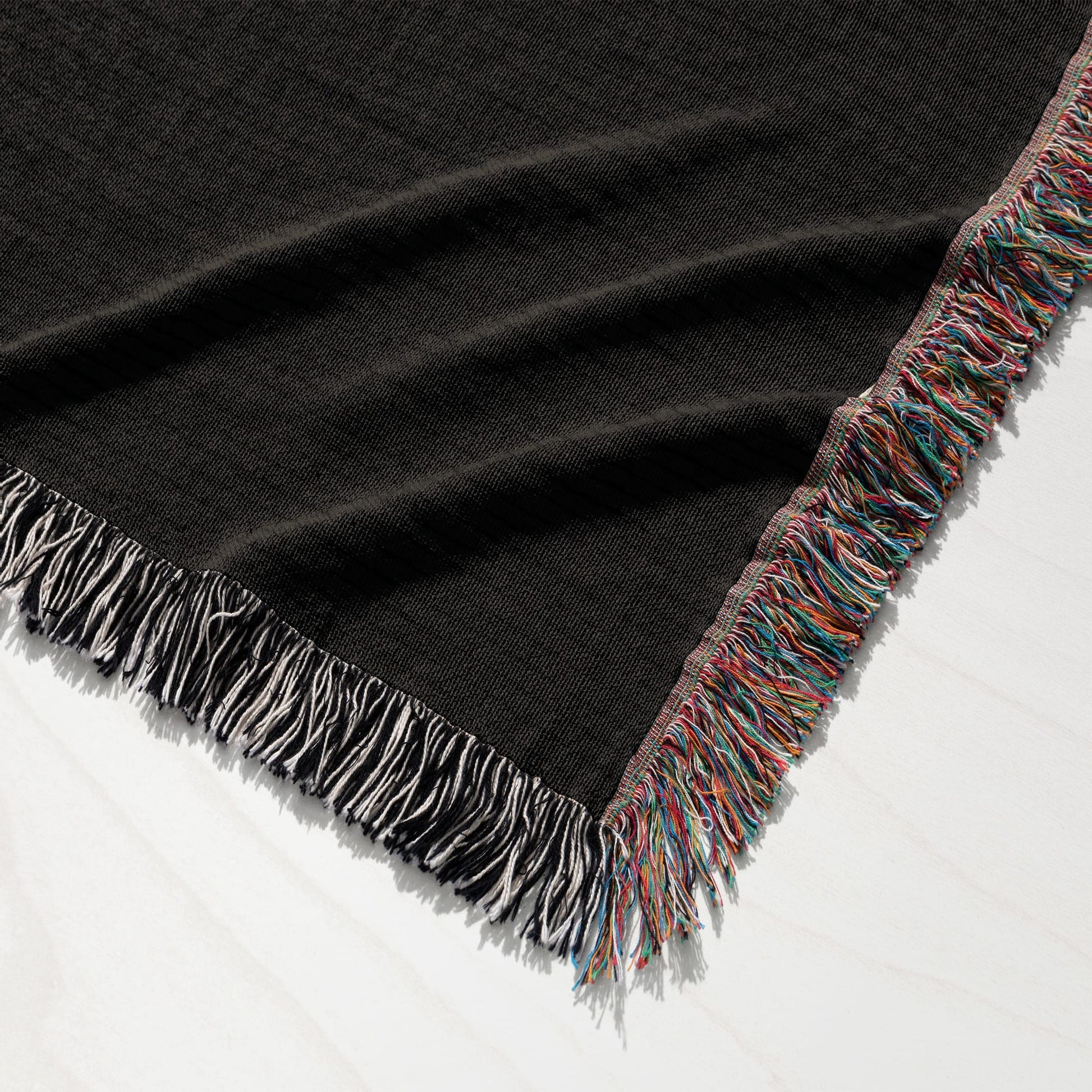 Dark throw blanket with multi-colored fringed edges, laid flat on a white surface.