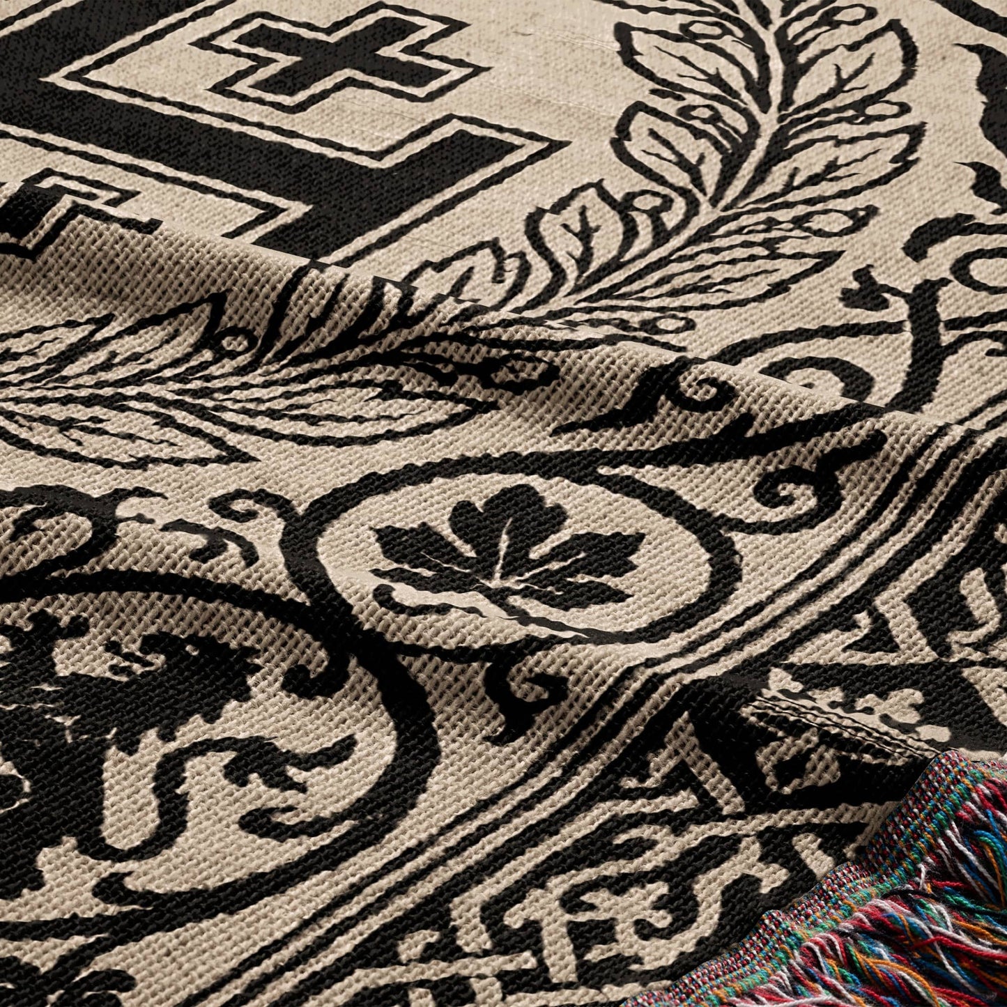 Woven blanket with black floral pattern on beige background and colorful fringe.
